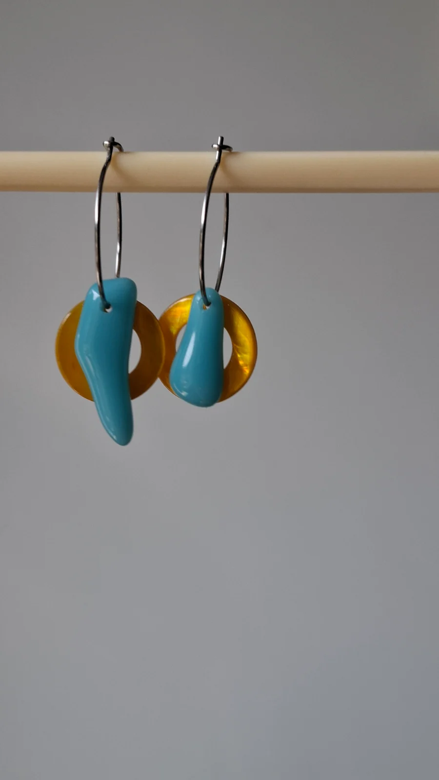 Boucles d'oreilles pendantes en verre bleu et anneaux jaunes posées sur un socle en bois