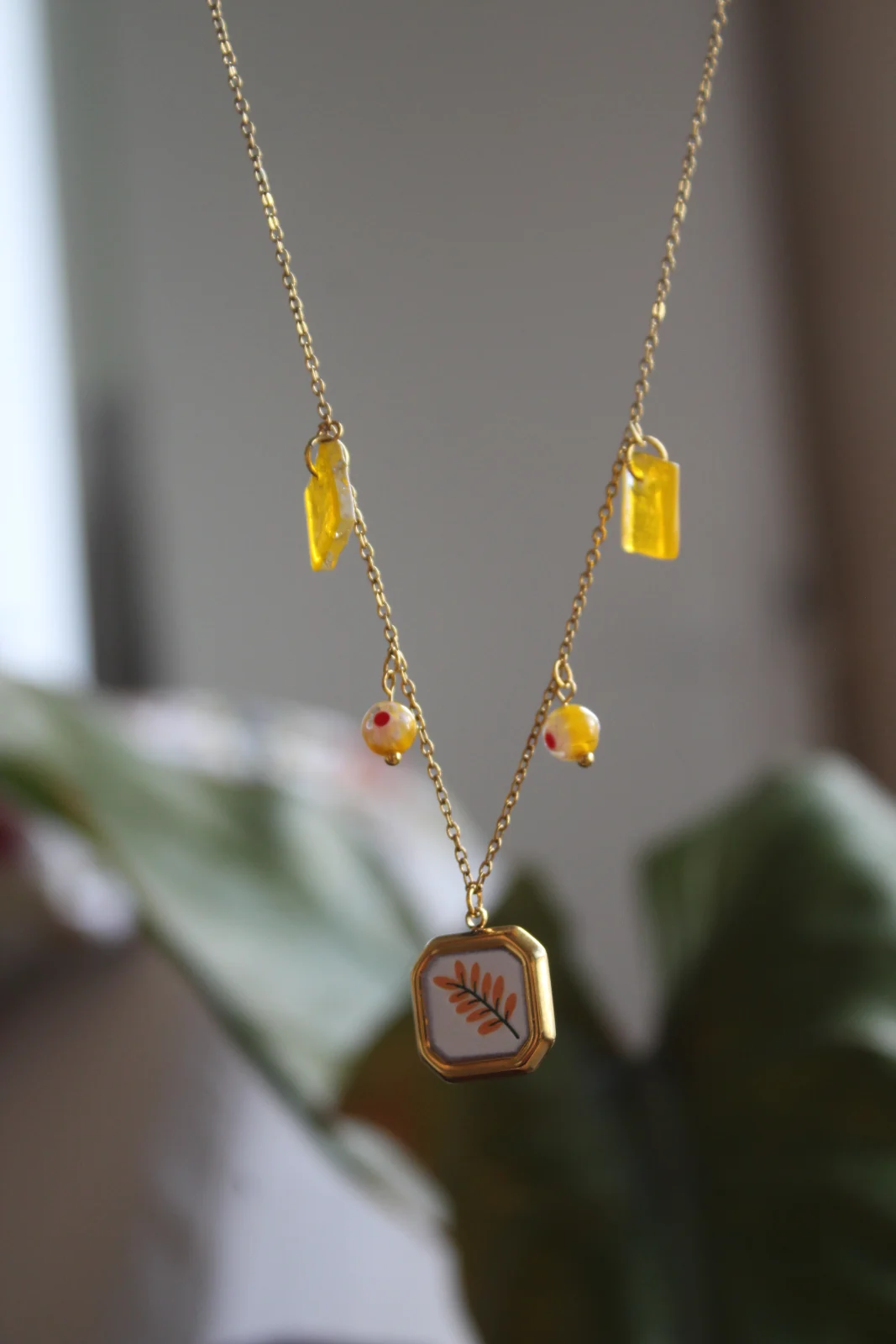 Gros plan sur le pendentif végétal octogonal et les pampilles jaunes sur chaîne fine dorée.