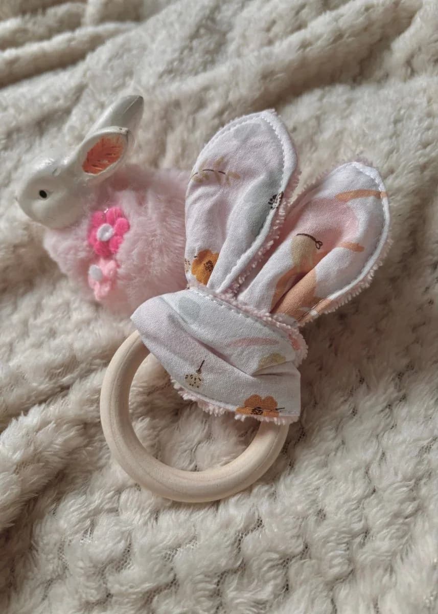 Anneau de dentition rond en bois avec tissu noué à motifs fleuris sur un plaid beige doux.
