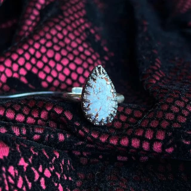 Bague en argent ornée d'une pierre magnésite taillée en goutte, posée sur un tissu en dentelle noire et rose.