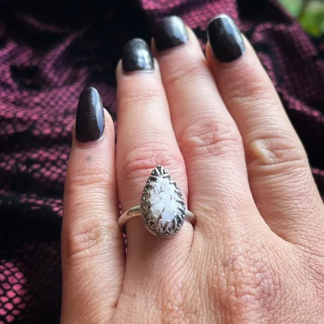 Bague argentée sertie d'une magnésite en forme de goutte, portée au doigt sur fond de tissu sombre.