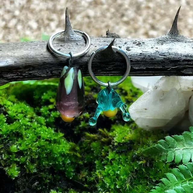 Boucles d'oreilles créoles suspendues à une branche épineuse au-dessus d'un lit de mousse végétale.