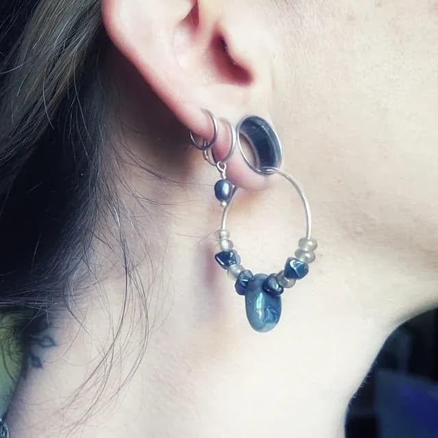 Créole Notte portée à l'oreille, ornée de perles de verre et d'une pierre d'agate aux tons gris et noirs.