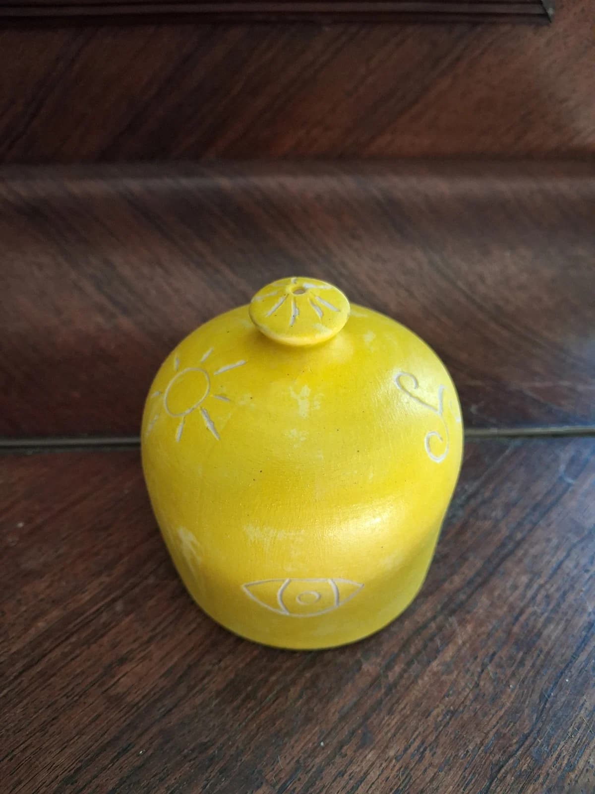 Objet en céramique jaune vif gravé de motifs de soleil et d'œil avec petite prise au sommet.