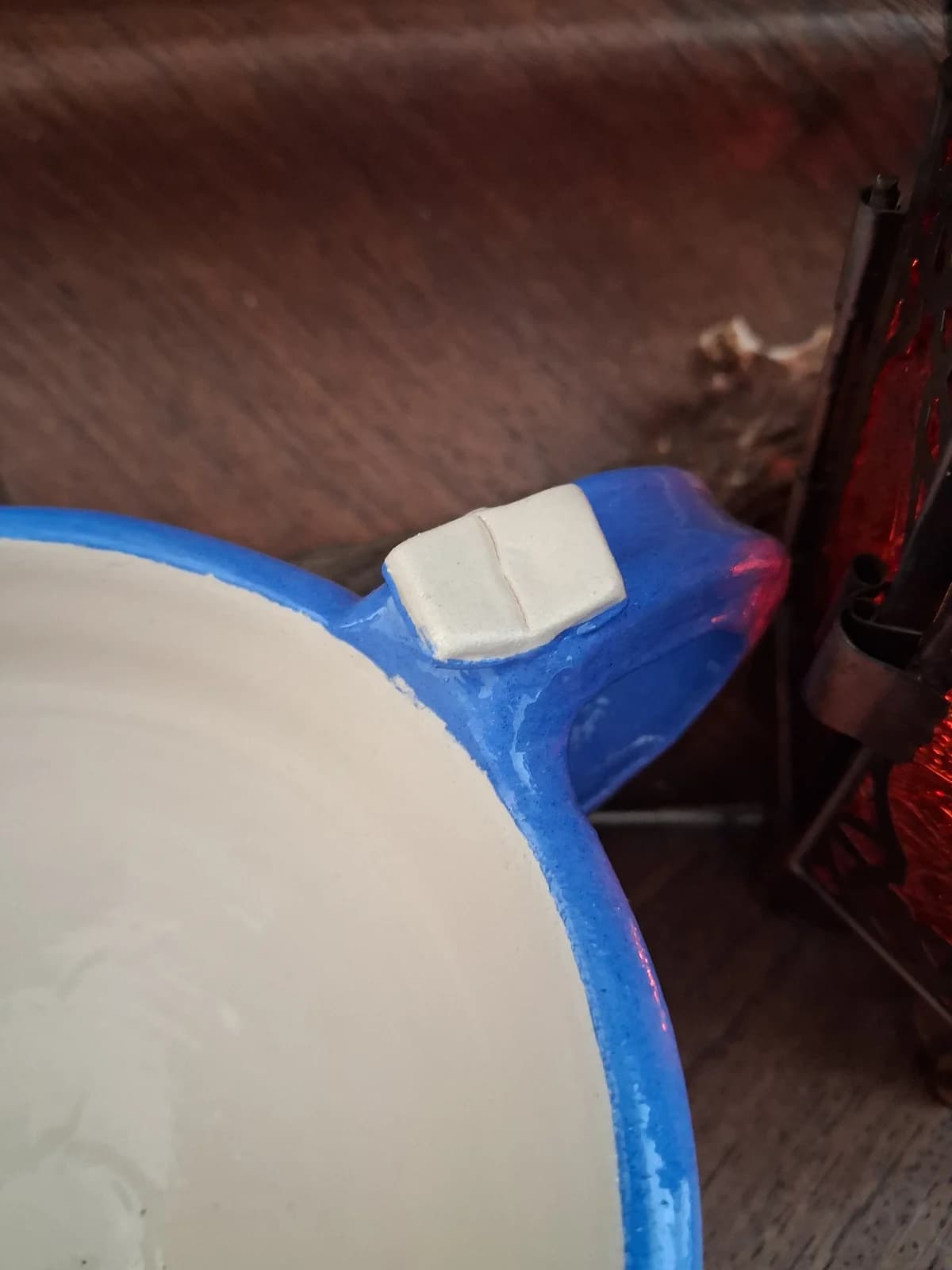 Gros plan sur l'anse bleue d'une tasse en céramique décorée d'un petit livre en relief blanc.