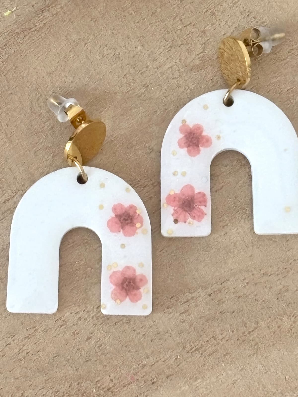 Gros plan sur les motifs floraux roses incrustés dans les boucles d'oreilles blanches.