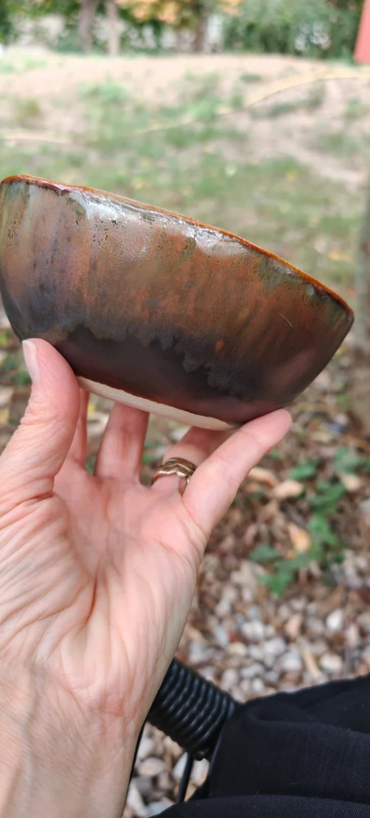 Bol artisanal en céramique aux émaux cuivrés et brun foncé tenu dans une main.