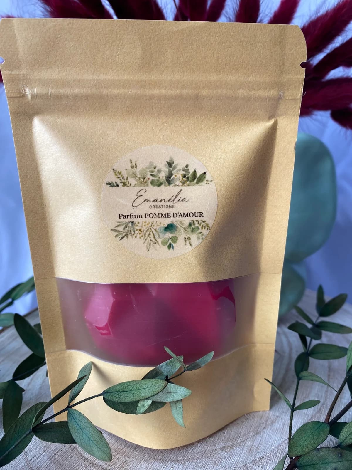 Gros plan sur le sachet kraft étiqueté Pomme d'amour laissant entrevoir le fondant rouge facetté.
