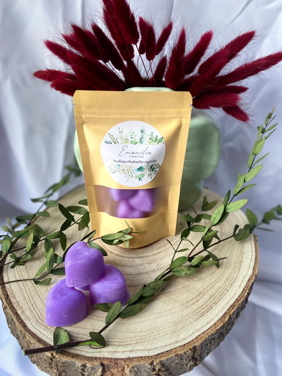 Sachet de fondants parfumés et cœurs violets disposés sur un rondin de bois décoré de feuillage.